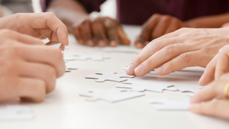 Group of hands collaborating on jigsaw puzzle at table