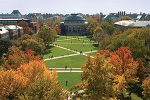 Aerial view of College of Law campus. Paths cut diagonally across a green field surrounded by deciduous trees in autumn.