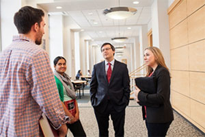 Diverse students speak with a faculty member in the hallway.