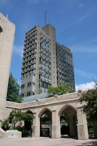 Law school exterior. In the foreground, a stone walkway with decorative arches. In the background, a gray skyscraper. 