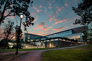 Law school exterior at sunset. Pink clouds hang over the building, which is flanked by tree silhouettes. A lit lampost stands at a crossroad leading up to the school.