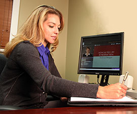 A woman sits at a computer and takes notes.