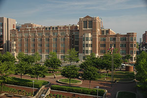 Law schol exterior--a brick building with beige accents. Many small deciduous trees and shrubs are scattered in a large courtyard that spans in front of the school.