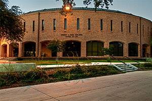 Exterior of School of Law's Ernest A. Rasa building. The building is round and made of brown brick. Open, arched entryways line its perimeter. Thin windows stand in a row above the arches.