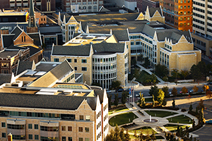 Aerial view of the university complex. Beige buildings with gray roofs are angled near a round, grassy courtyard that has paths leading away from it like spokes.
