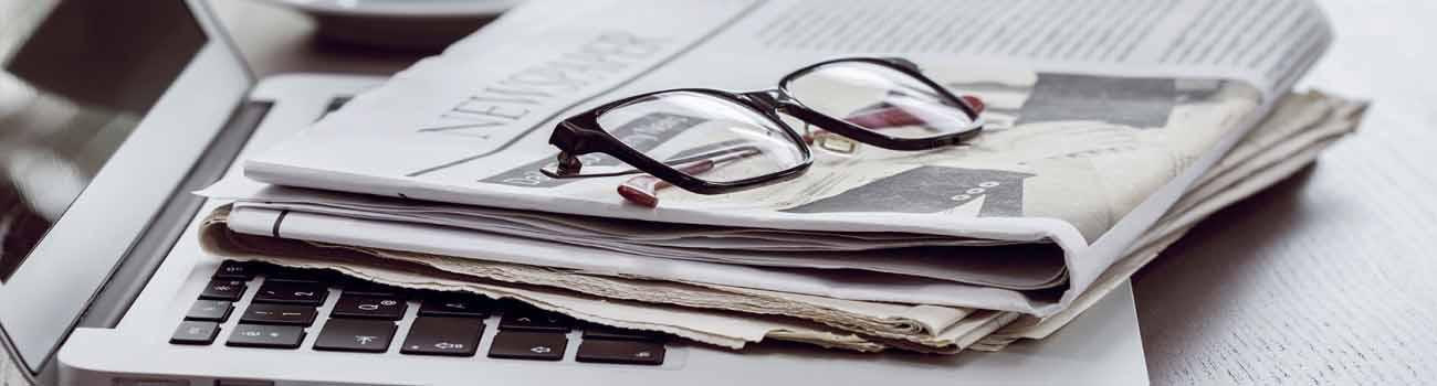 Reading glasses lying on top of newspaper and laptop.