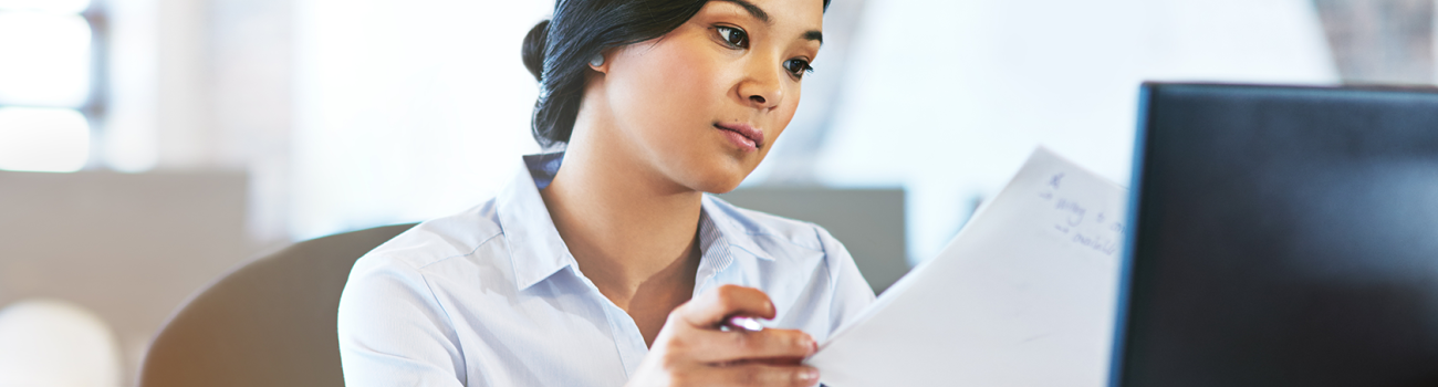 Student looking at papers in front of computer monitor