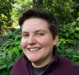 A headshot of a woman with short dark hair wearing a plum colored shirt