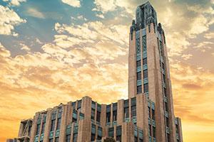 The law school building's spire juts into the golden, cloudy sky at sunset.