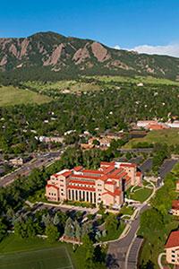 Aerial view of university building. Trees surround the campus grounds. Mountains are in view.