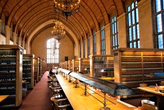 A view inside Myron Taylor Hall Library showing rows of wooden bookcases flanking a long central table with reading lamps down the center.