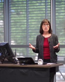 Professor behind desk speaking to class