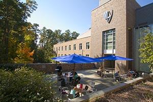 Students sit at patio tables underneath umbrellas