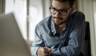 person working on laptop and taking notes