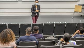A woman wearing a face mask gives a presentation to a live audience