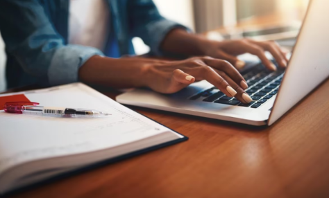person at laptop with pen and pad