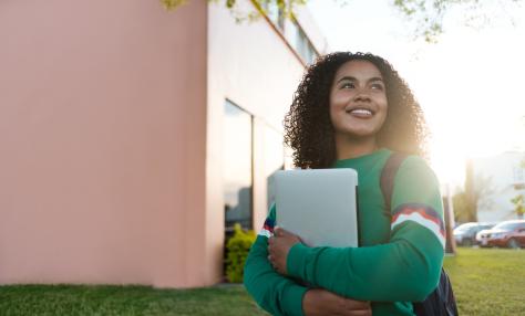 A student holds books and walks through campus