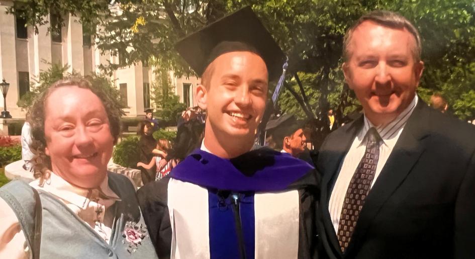 A man stands between his parents at his law school graduation
