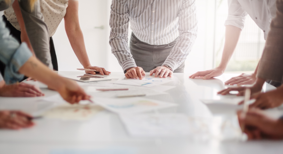 A group of people stand around a table that's covered in papers