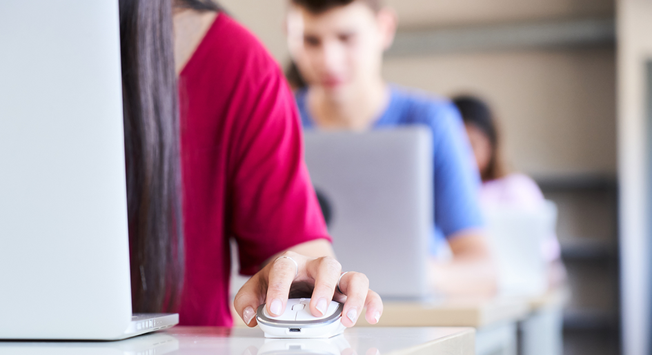 Students sit in a line of desks, typing on computers