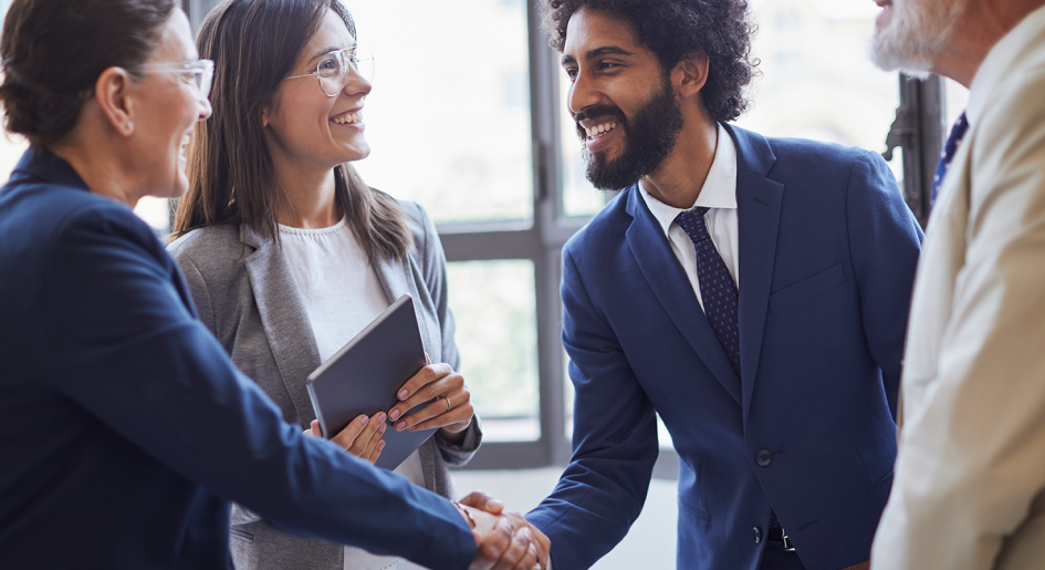 A group of people in business professional clothing stand in a circle as two of them shake hands
