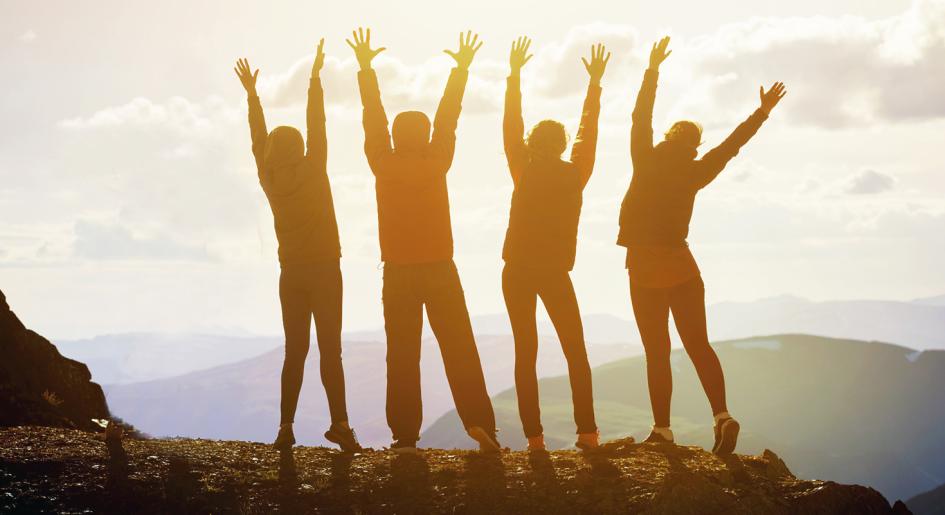 Sunlit silhouettes of people raising their arms on a mountaintop