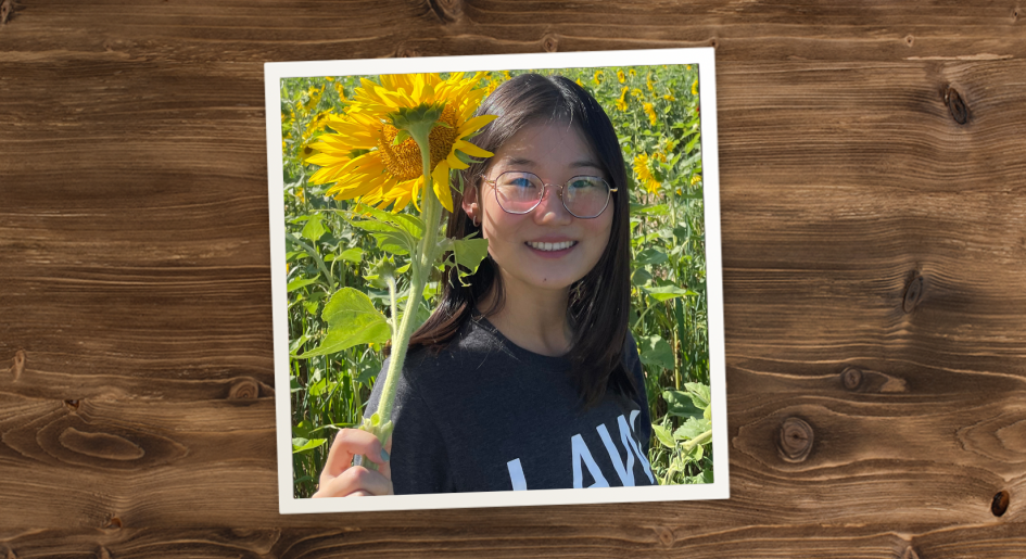 Bingram Li standing in a field of sunflowers, holding a sunflower and smiling.