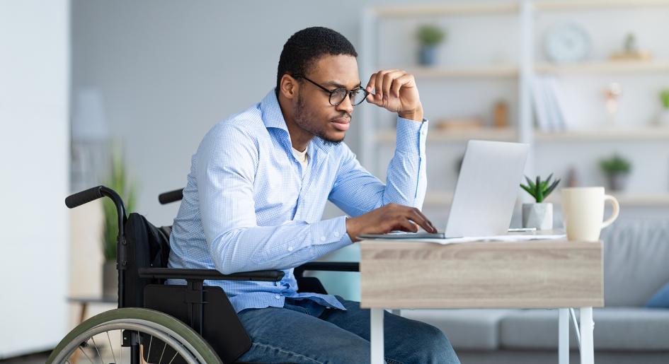 Person in wheelchair using laptop at desk