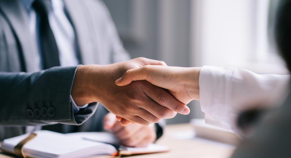 Two people shake hands over a desk