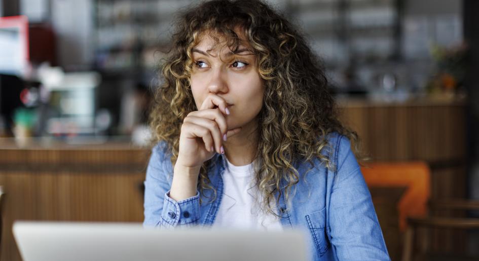 A woman sits at a laptop with a pensive look on her face