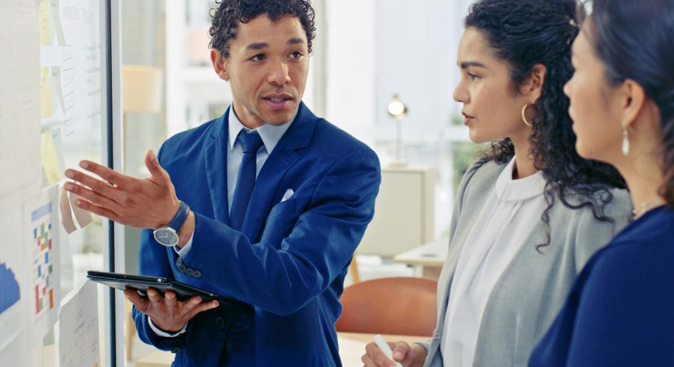 Three people stand and look at a whiteboard covered in papers