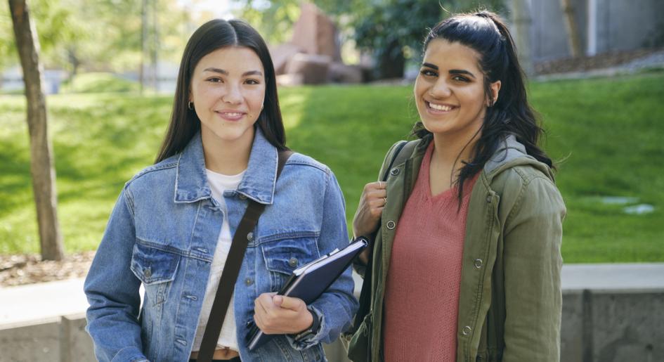 Two students standing on campus, smiling at camera
