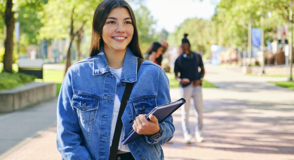 Law student standing on walkway with books in hand, smiling