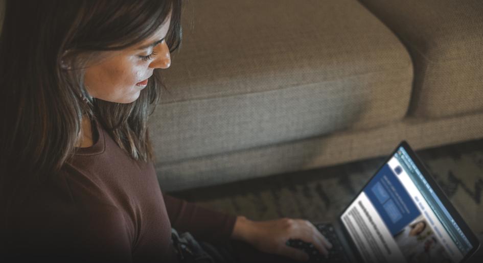 A woman sits on the floor, looking at a laptop. LSAC.org is pulled up on the laptop. 