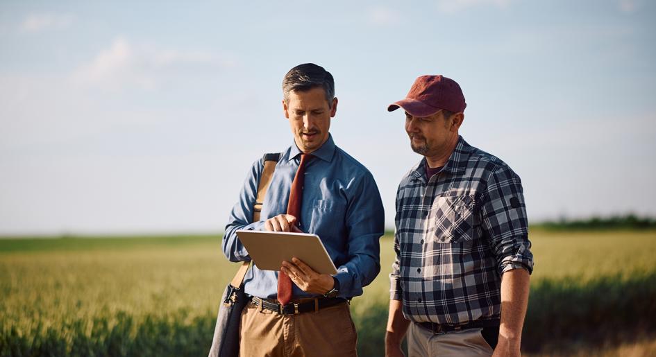 Two people talking outside near farm field.