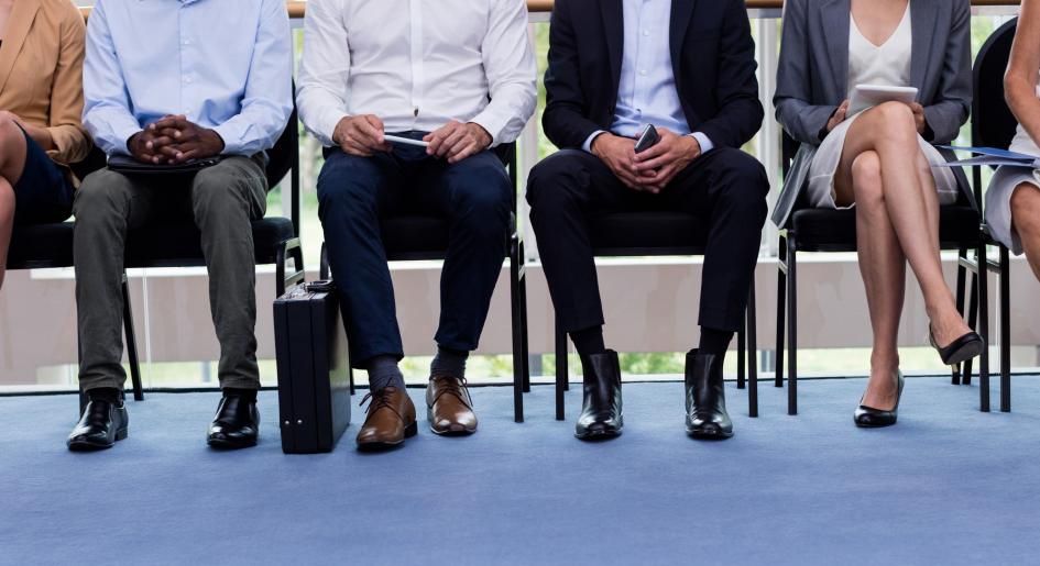 A group of people wearing professional clothing sit in a line of chairs