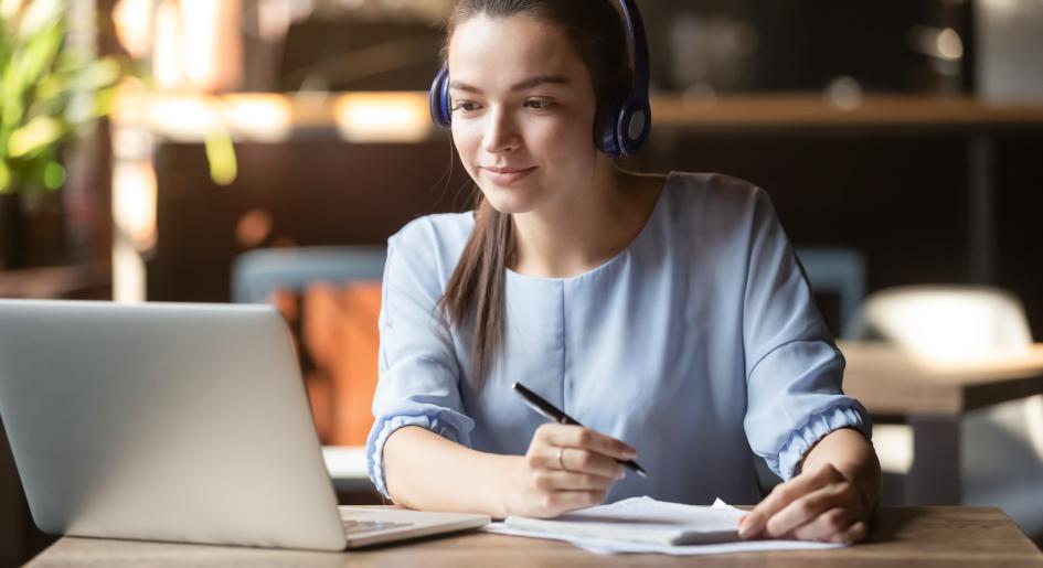 Person at laptop with headphones taking notes