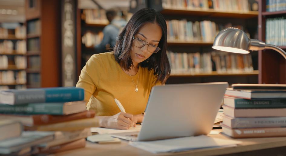 Law student in library with laptop open, taking notes