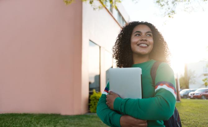 A student holds books and walks through campus