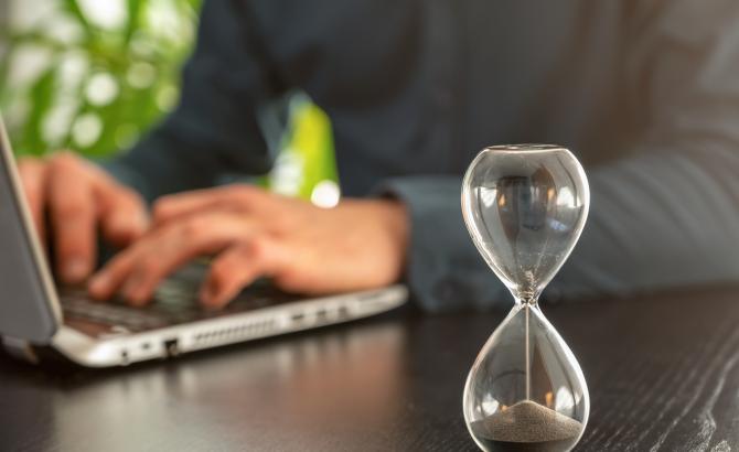 Someone types on a computer with an hour glass next to them