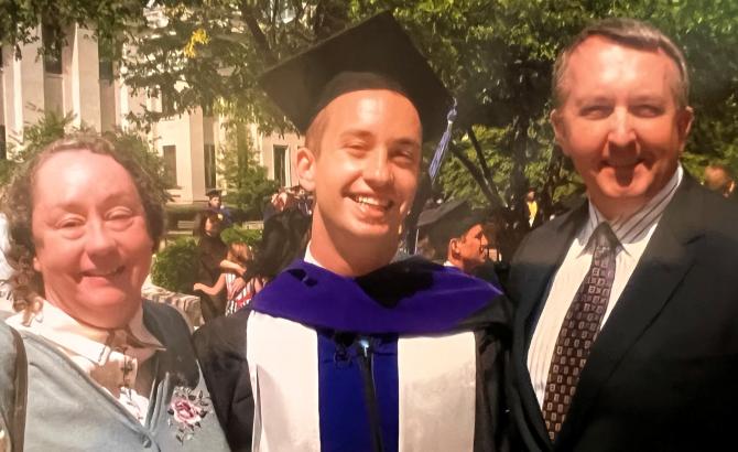 A man stands between his parents at his law school graduation