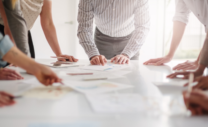 A group of people stand around a table that's covered in papers