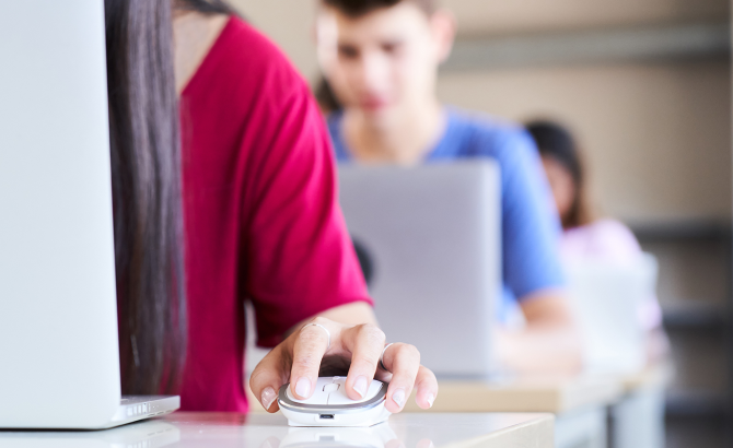 Students sit in a line of desks, typing on computers