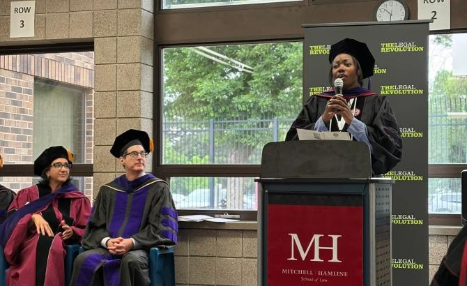 A woman speaks at a podium at a law school graduation