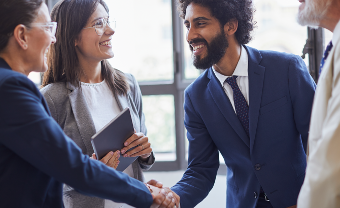 A group of people in business professional clothing stand in a circle as two of them shake hands