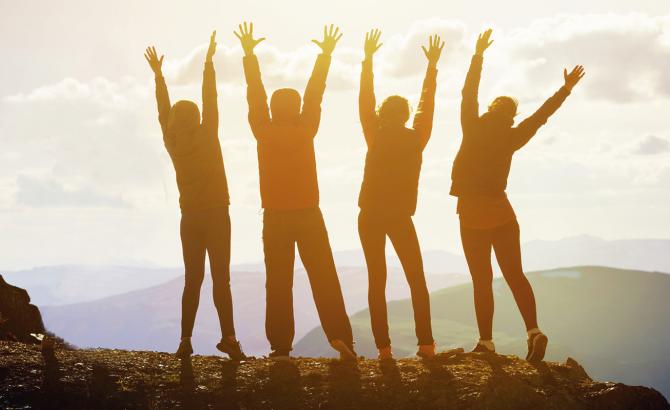 Sunlit silhouettes of people raising their arms on a mountaintop