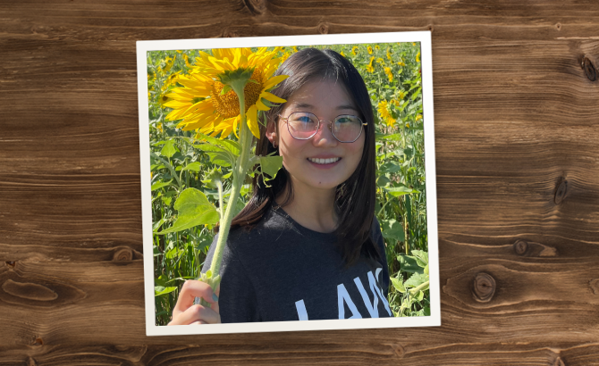 Bingram Li standing in a field of sunflowers, holding a sunflower and smiling.