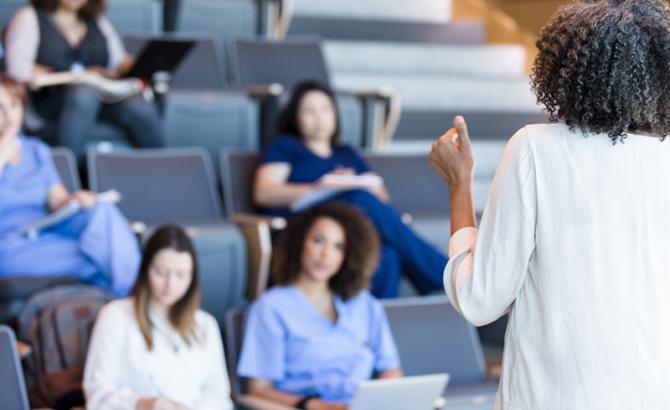 Students sitting in a classroom while a teacher presents. 