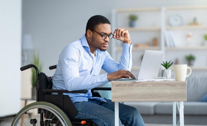 Person in wheelchair using laptop at desk