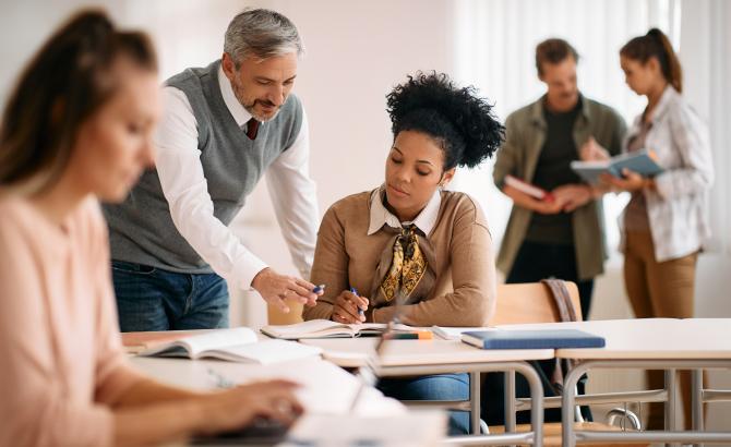 A teacher leans over a student's desk, helping them